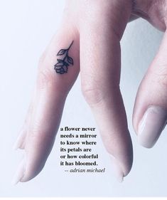 a person's hand with a small flower tattoo on the middle finger and an inspirational quote above it