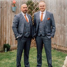 two men in suits standing next to each other on grass near fence and flower pot