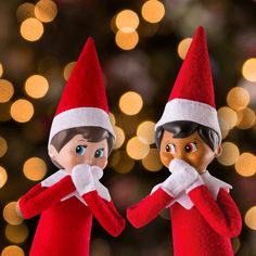 two elfs standing next to each other in front of a christmas tree