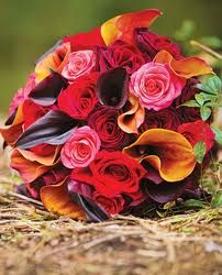 a bridal bouquet with red, orange and pink flowers on the ground next to straw