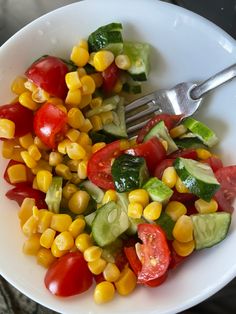 a white bowl filled with corn, tomatoes and cucumber on top of a table