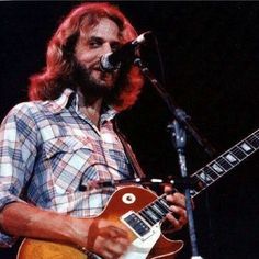 a man with long hair and beard playing an electric guitar in front of a microphone