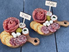 two figurines made out of meats and cheese on wooden platters with name tags