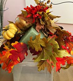 an arrangement of autumn leaves and acorns in a vase on a table top