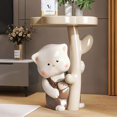 a white cat figurine sitting on top of a table next to a potted plant