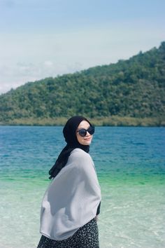 a woman standing on top of a beach next to the ocean wearing a hijab