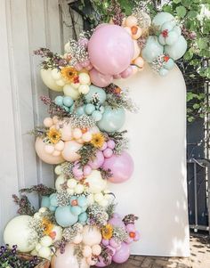 a bunch of balloons hanging from the side of a wall next to flowers and plants