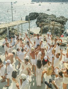 a group of people standing around each other in front of the ocean and some boats