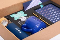 an open box with items in it including a blue coffee mug, pen and paper