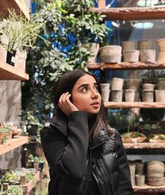 a woman is talking on her cell phone in a store filled with potted plants