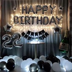 a happy birthday sign surrounded by balloons and streamers in front of a curtained backdrop