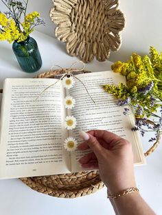 a person is holding an open book with daisies on it and some yellow flowers