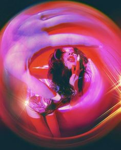 a woman with long hair is posing in front of a red and purple light while holding her hand up to her face