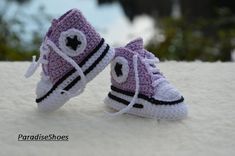 two crocheted purple sneakers are sitting on the white surface with trees in the background