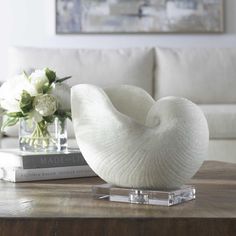 a white sculpture sitting on top of a wooden table next to a book and vase