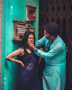 a woman in a blue sari standing next to a man who is touching his face