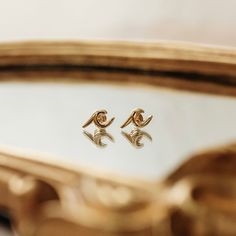 two gold earrings sitting on top of a mirror