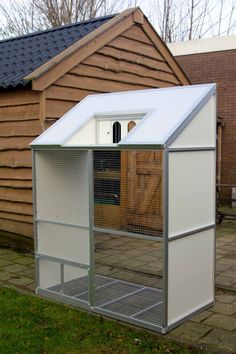 a small white chicken coop sitting on top of a brick patio next to a house