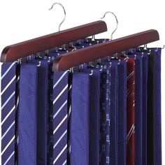 several ties are hanging on wooden hangers in front of blue shirts and purple ones