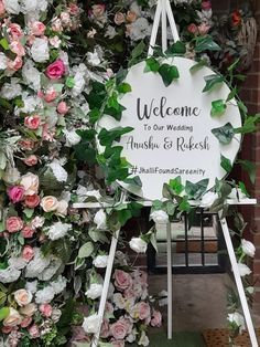 a welcome sign surrounded by flowers in front of a wall with greenery on it