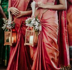 two women dressed in red sari and holding small lanterns with white flowers on them