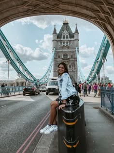 a woman sitting on top of a trash can in front of a bridge