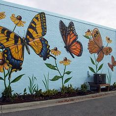 a painted mural on the side of a building with yellow and black butterflies flying over flowers