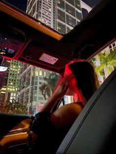 a woman sitting in the back seat of a car at night with city lights behind her