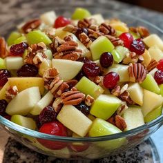 a glass bowl filled with apples, cranberries and pecans on top of a granite counter