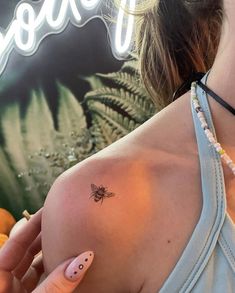 a woman with a bee tattoo on her left shoulder and right hand holding an orange