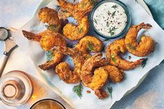 fried shrimp with dipping sauce on a white platter next to two glasses of beer