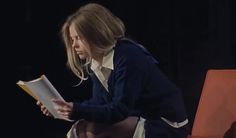 a woman sitting on a chair holding a book in her hands and looking at it