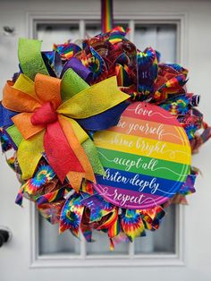 a colorful wreath hanging from the side of a door with a rainbow ribbon on it