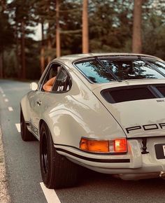 an old porsche sits parked on the side of the road in front of some trees