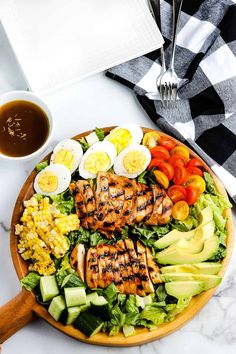 a salad with chicken, avocado, tomatoes and eggs on it next to a cup of coffee