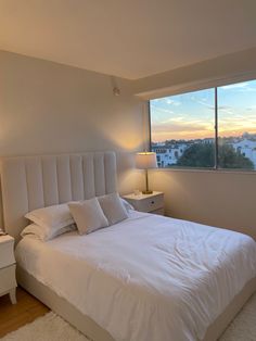 a bedroom with a bed, nightstand and large window overlooking the city skyline at sunset