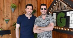 two men standing next to each other in front of a wooden wall with letters on it