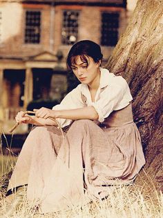 a woman sitting on the ground next to a tree