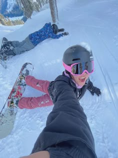 two people laying in the snow with their skis on and one person wearing goggles