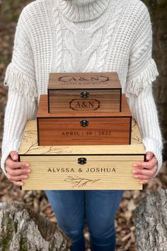 a woman holding three wooden boxes in front of her face and wearing a white sweater