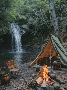 there is a tent next to a fire in the woods with a waterfall behind it