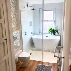 a white bath tub sitting next to a toilet in a bathroom under a window on top of a hard wood floor