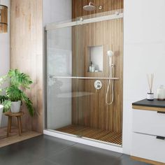 a bathroom with a glass shower door and wood paneling on the wall next to a plant