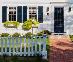 a white house with blue shutters and green plants on the front lawn, along with a brick walkway