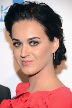 a close up of a person wearing a red dress and smiling at the camera with her hair in a bun