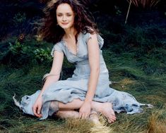 a woman in a blue dress sitting on the ground with her hair blowing in the wind