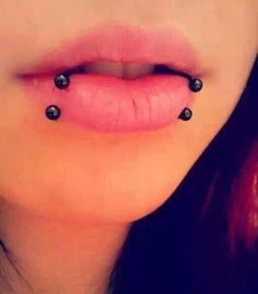 a woman's tongue with black balls attached to the top of her lip and nose