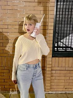 a woman standing in front of a brick wall talking on a cell phone while wearing jeans