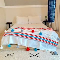 a white bed with red, blue and green pom poms on it