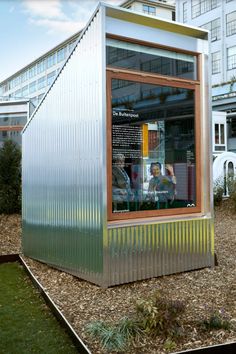 a small metal structure sitting in the middle of a field next to tall buildings and grass